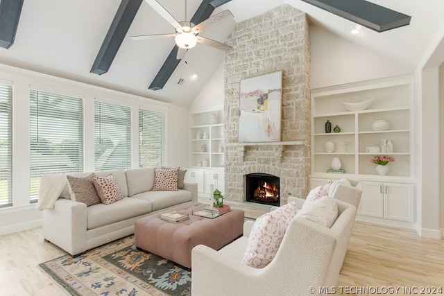 living room featuring light wood-type flooring, high vaulted ceiling, built in shelves, ceiling fan, and a stone fireplace