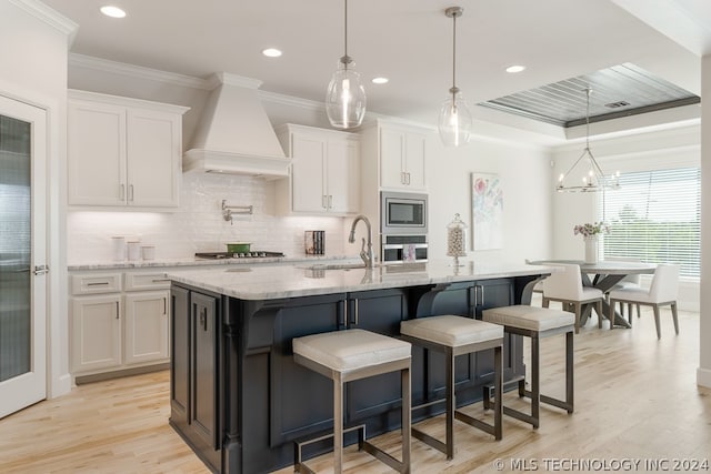 kitchen with a center island with sink, custom exhaust hood, and white cabinetry