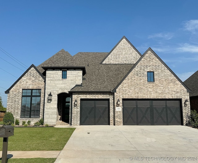 french country inspired facade with brick siding, a shingled roof, stone siding, driveway, and a front lawn