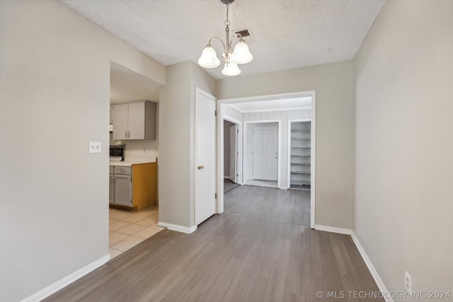 unfurnished dining area featuring light wood-type flooring, a chandelier, and a textured ceiling