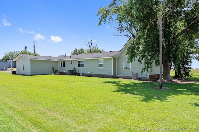 rear view of house with central AC unit and a lawn