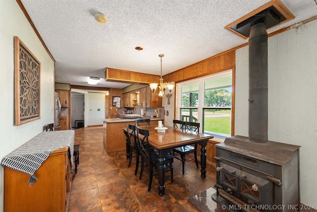 dining space featuring an inviting chandelier, wood walls, a textured ceiling, and a wood stove