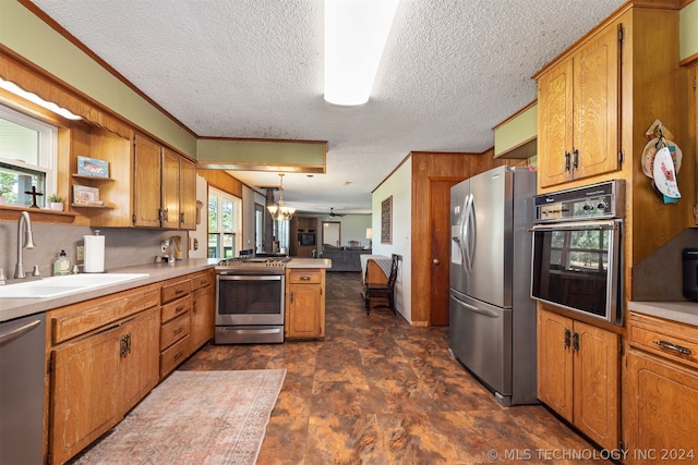 kitchen with appliances with stainless steel finishes, decorative light fixtures, sink, kitchen peninsula, and crown molding