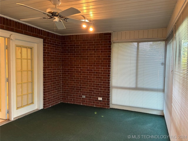 carpeted spare room featuring ceiling fan and brick wall