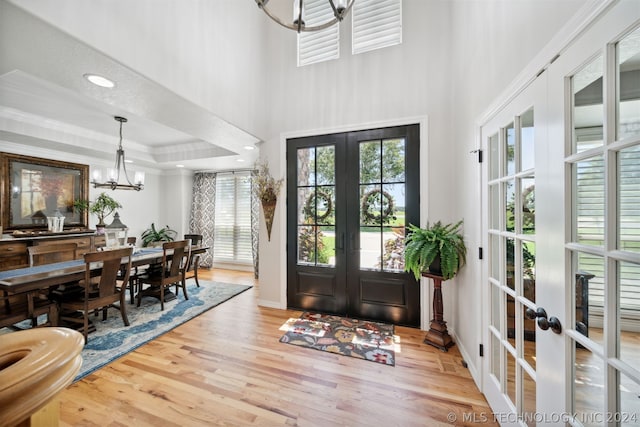 entrance foyer featuring french doors, hardwood / wood-style floors, ornamental molding, a tray ceiling, and a notable chandelier