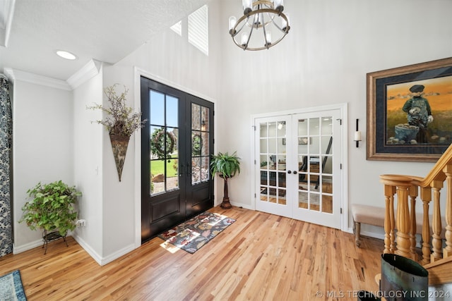 foyer featuring a chandelier, a high ceiling, french doors, light hardwood / wood-style floors, and ornamental molding