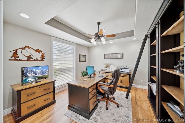 office featuring ceiling fan, light hardwood / wood-style flooring, and a tray ceiling