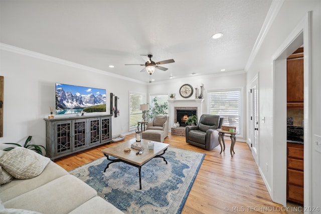 living room with ceiling fan, ornamental molding, a fireplace, a textured ceiling, and light hardwood / wood-style flooring