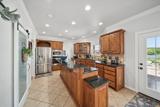 kitchen with a center island, dark stone countertops, a barn door, appliances with stainless steel finishes, and ornamental molding