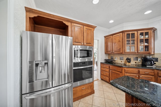 kitchen with backsplash, crown molding, dark stone counters, appliances with stainless steel finishes, and light tile patterned flooring