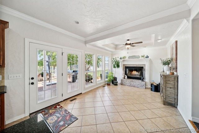 tiled living room featuring ornamental molding, a healthy amount of sunlight, a brick fireplace, and a tray ceiling