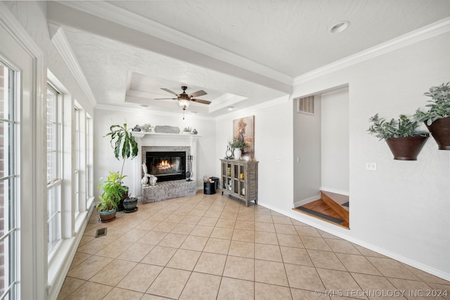 tiled living room featuring ornamental molding, ceiling fan, a tray ceiling, and a fireplace