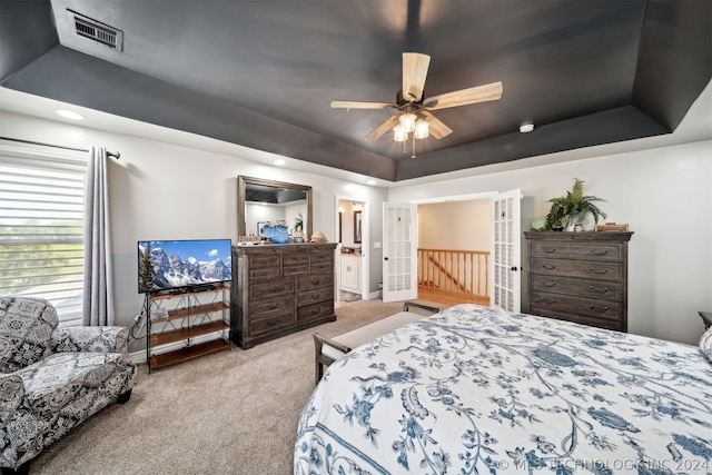 bedroom featuring a raised ceiling, light colored carpet, ceiling fan, and connected bathroom