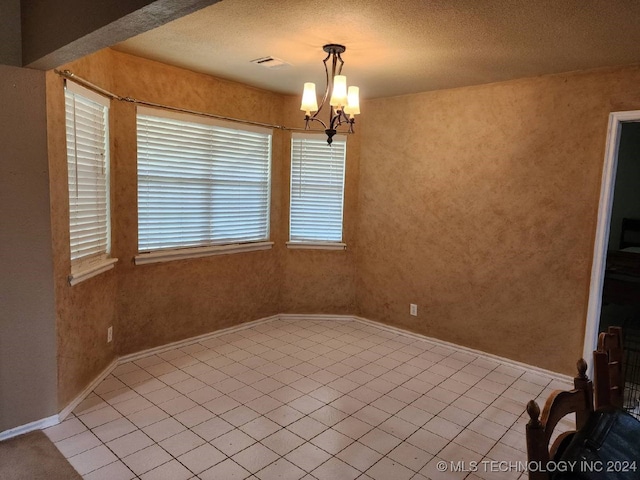 tiled spare room with a chandelier and a textured ceiling