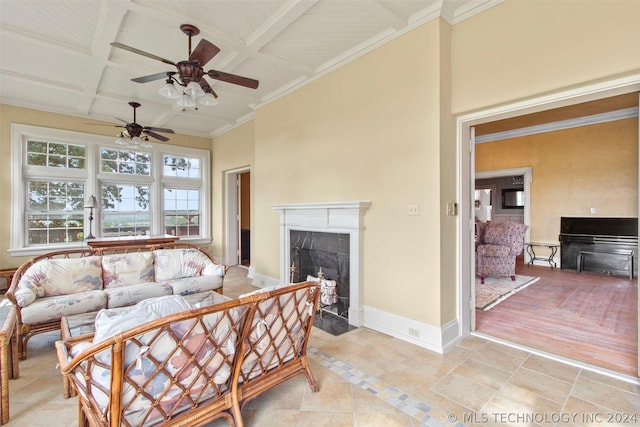 living room with coffered ceiling, ceiling fan, a premium fireplace, ornamental molding, and beamed ceiling