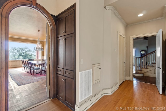 corridor with a notable chandelier, light wood-type flooring, and ornamental molding