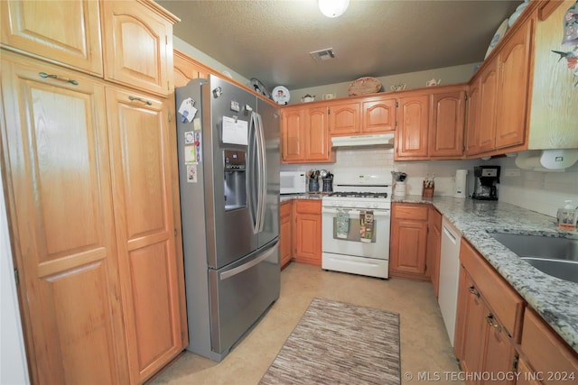 kitchen with tasteful backsplash, light stone counters, sink, and white appliances