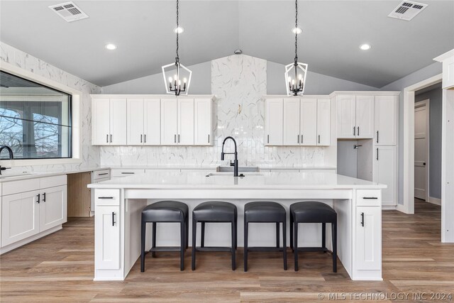 kitchen featuring vaulted ceiling, hanging light fixtures, light hardwood / wood-style flooring, and a center island with sink