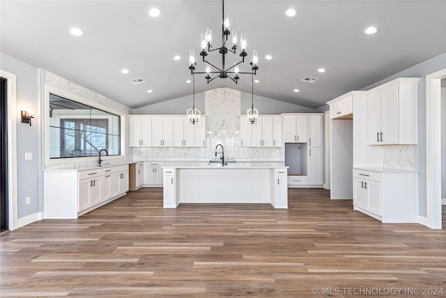 kitchen with sink, vaulted ceiling, white cabinets, and a center island with sink