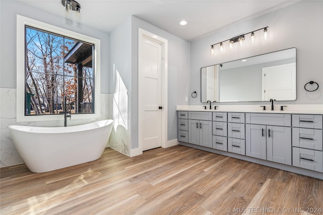 full bath featuring a freestanding tub, double vanity, a sink, and wood finished floors