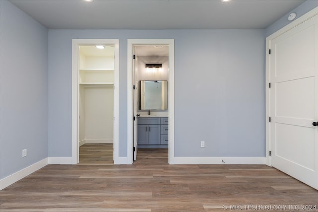 unfurnished bedroom with ensuite bath, a spacious closet, light hardwood / wood-style floors, and a closet