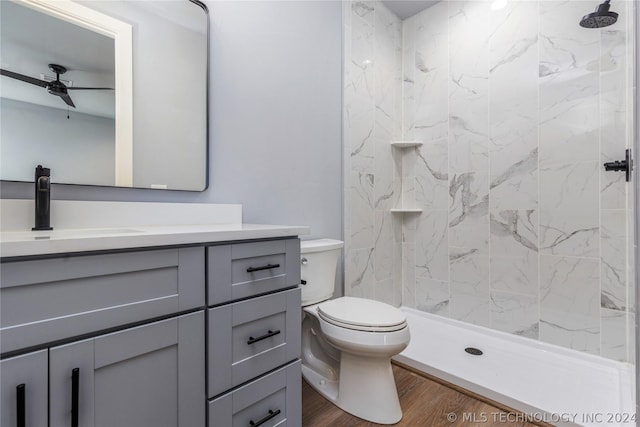 bathroom with hardwood / wood-style flooring, vanity, tiled shower, ceiling fan, and toilet