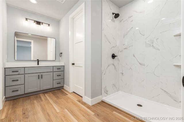 bathroom featuring a tile shower, vanity, recessed lighting, wood finished floors, and baseboards