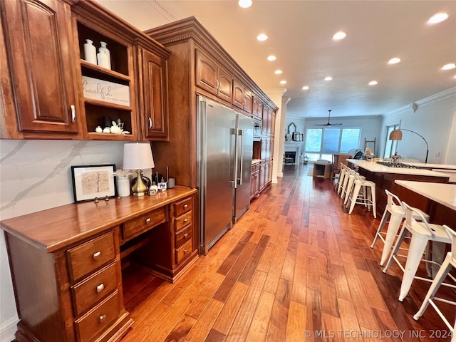 kitchen featuring built in desk, ornamental molding, built in fridge, ceiling fan, and light hardwood / wood-style floors