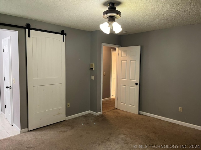 unfurnished bedroom with ceiling fan, light colored carpet, a barn door, and a textured ceiling