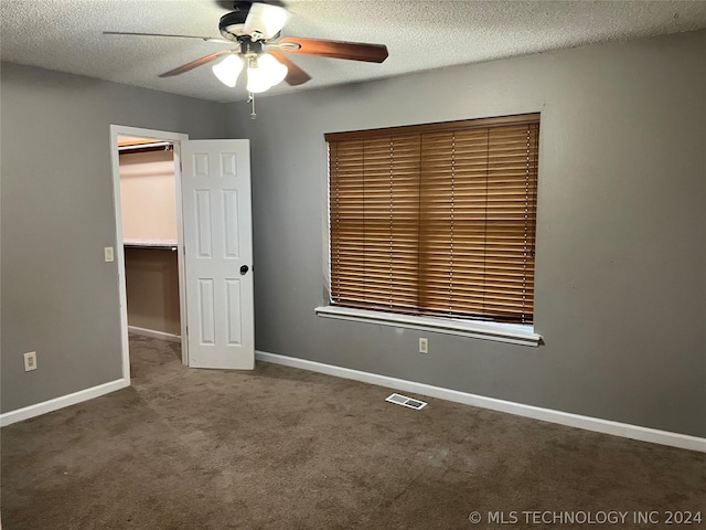 unfurnished bedroom featuring a closet, dark colored carpet, ceiling fan, a textured ceiling, and a walk in closet