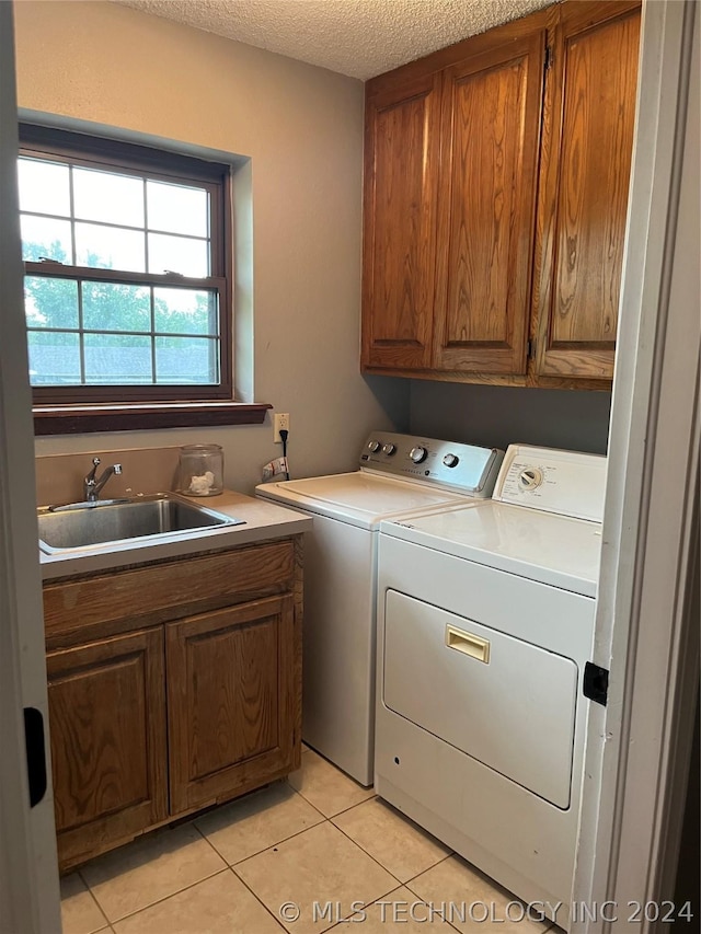 clothes washing area with sink, a textured ceiling, cabinets, light tile patterned floors, and separate washer and dryer