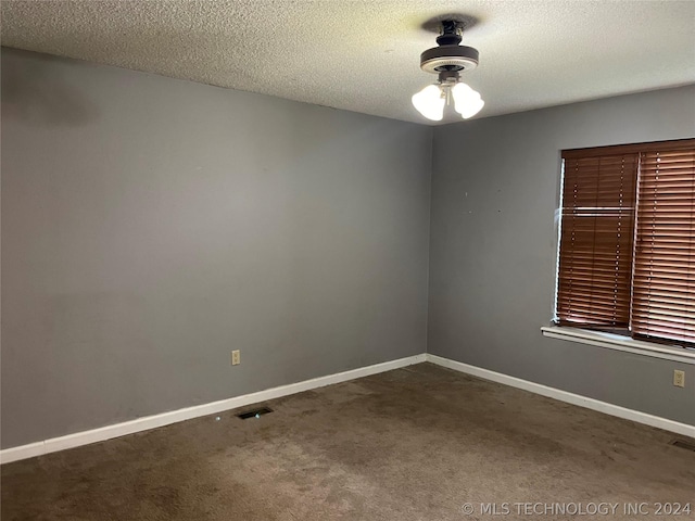 unfurnished room featuring a textured ceiling and dark colored carpet