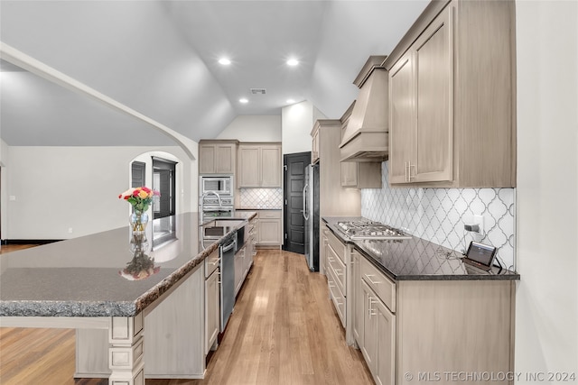 kitchen with stainless steel appliances, vaulted ceiling, light hardwood / wood-style floors, backsplash, and custom exhaust hood