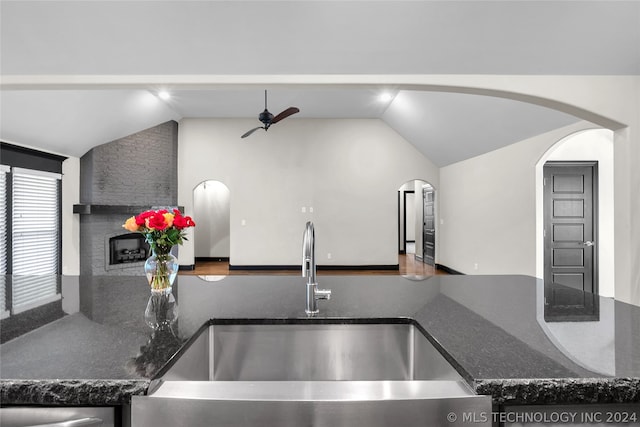 kitchen with a stone fireplace, hardwood / wood-style flooring, vaulted ceiling, and dark stone counters