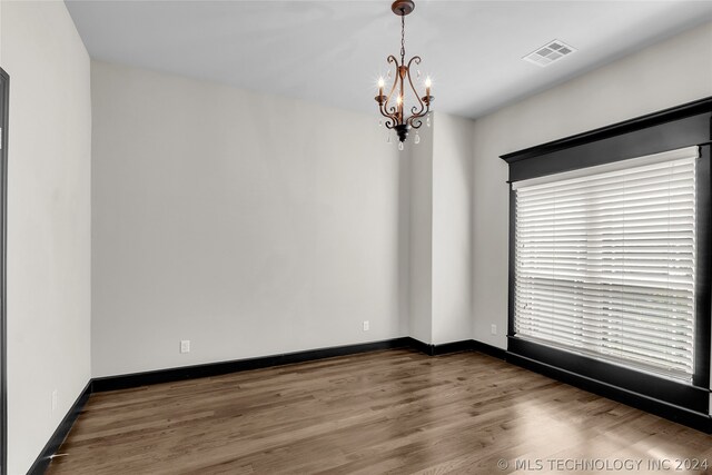 spare room with an inviting chandelier and wood-type flooring