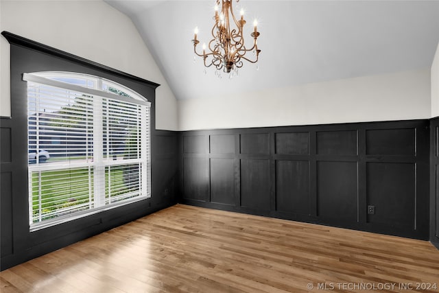 empty room with vaulted ceiling, an inviting chandelier, and light hardwood / wood-style floors