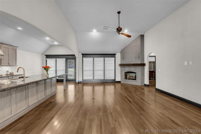 unfurnished living room with a large fireplace, hardwood / wood-style flooring, ceiling fan, brick wall, and sink