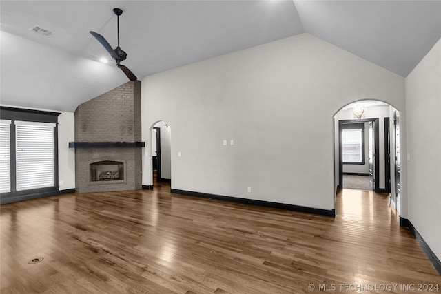 unfurnished living room with a fireplace, hardwood / wood-style flooring, ceiling fan, high vaulted ceiling, and brick wall