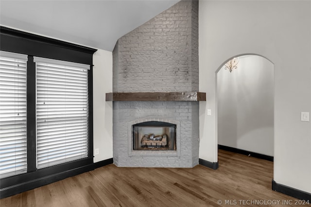 unfurnished living room featuring plenty of natural light, lofted ceiling, wood-type flooring, and a large fireplace