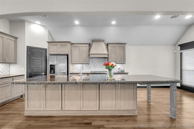 kitchen with lofted ceiling, tasteful backsplash, stainless steel appliances, custom exhaust hood, and a center island with sink