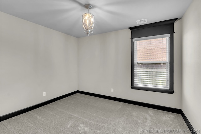 carpeted empty room featuring an inviting chandelier