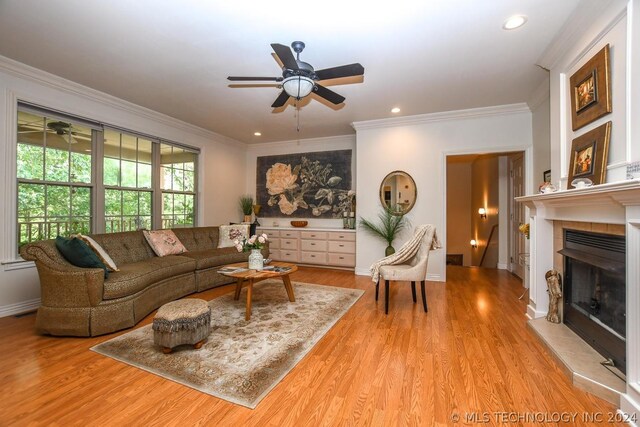 living room featuring a tiled fireplace, crown molding, ceiling fan, and light wood-type flooring