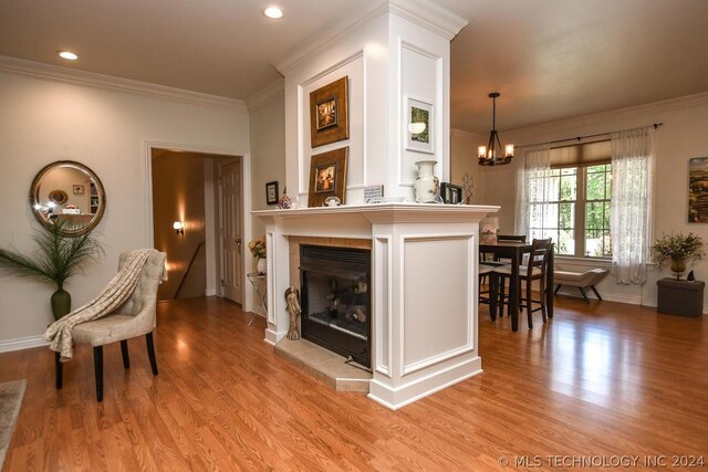 living room featuring crown molding, a tiled fireplace, light hardwood / wood-style flooring, and a notable chandelier