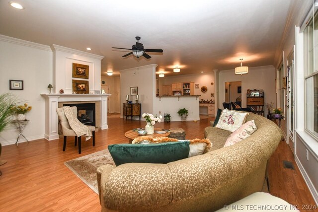 living room with hardwood / wood-style flooring, a multi sided fireplace, ornamental molding, and ceiling fan