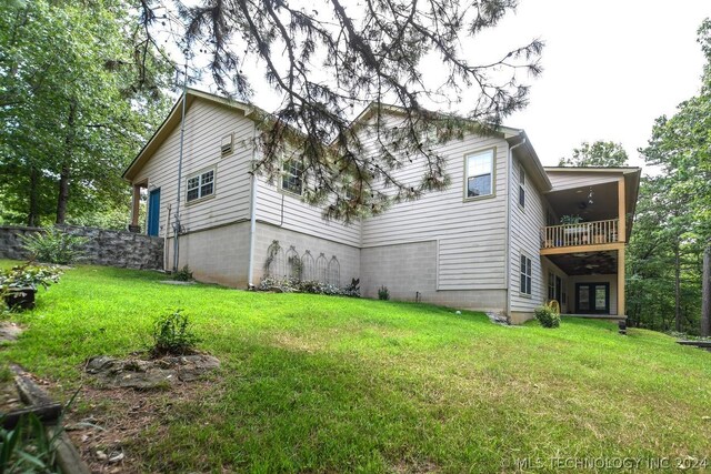 rear view of property featuring ceiling fan, a balcony, and a lawn