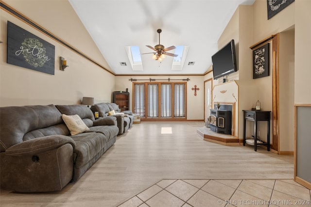 living room with light wood-type flooring, a wood stove, ceiling fan, and lofted ceiling with skylight