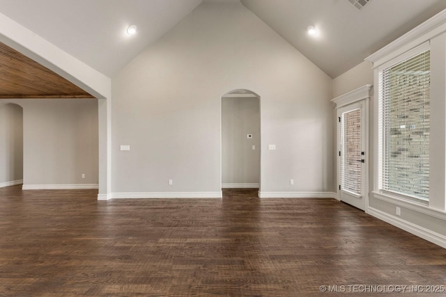 empty room featuring high vaulted ceiling, arched walkways, dark wood finished floors, and baseboards