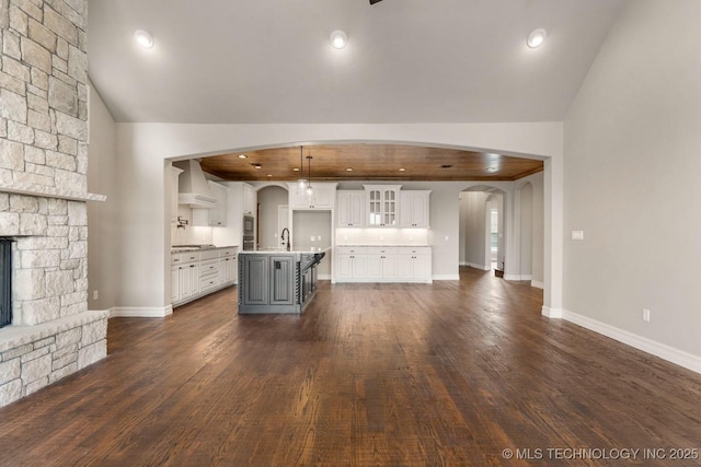 kitchen featuring a center island with sink, arched walkways, a stone fireplace, white cabinetry, and a sink