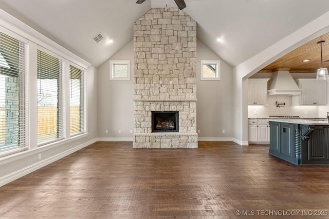 unfurnished living room with dark wood finished floors, visible vents, a stone fireplace, high vaulted ceiling, and baseboards