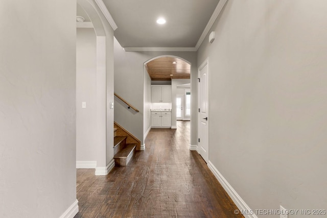 hallway with arched walkways, crown molding, stairway, dark wood-type flooring, and baseboards